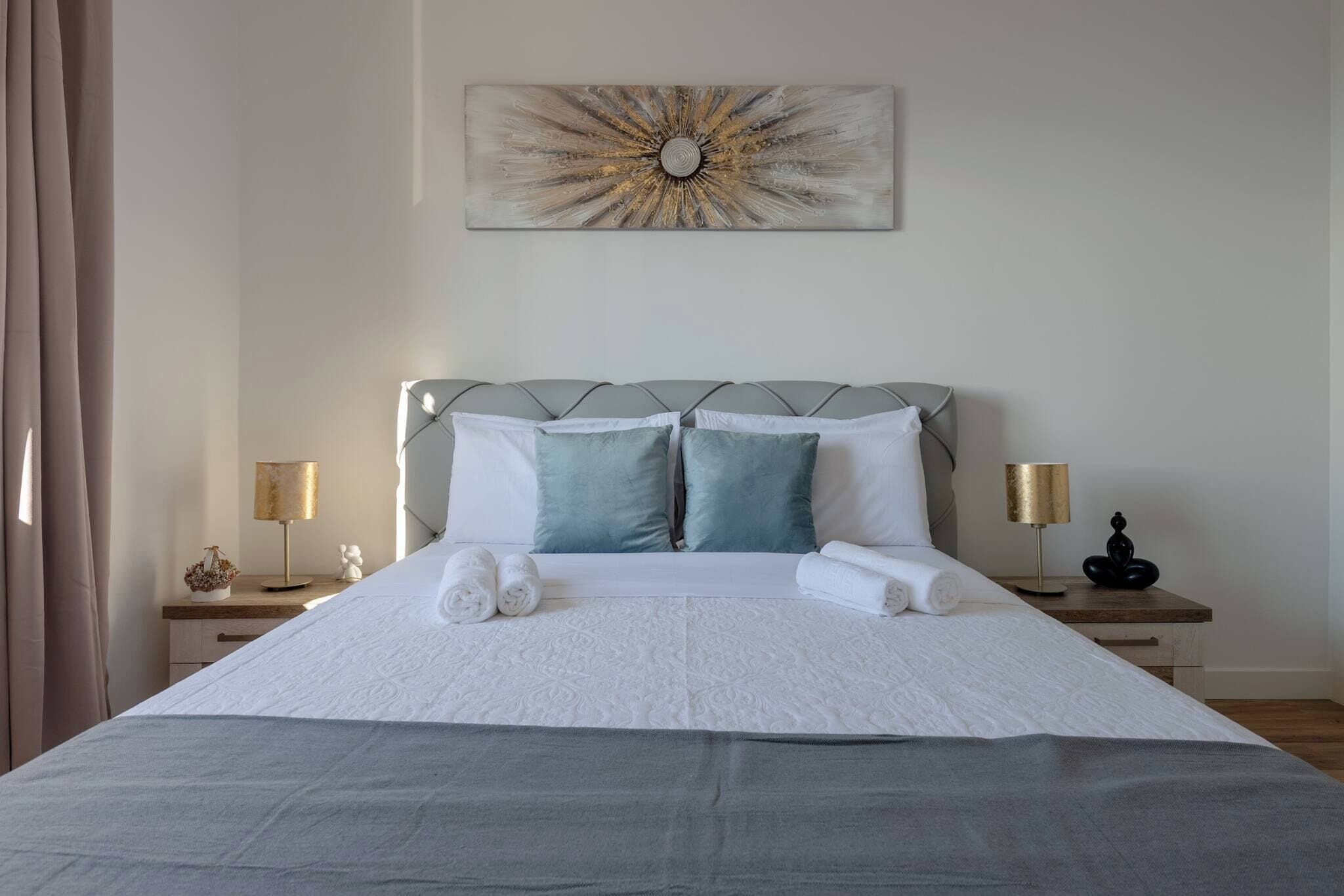 Un letto rifatto con lenzuola bianche e due cuscini, un elemento decorativo sulla parete sopra e lampade ai comodini.