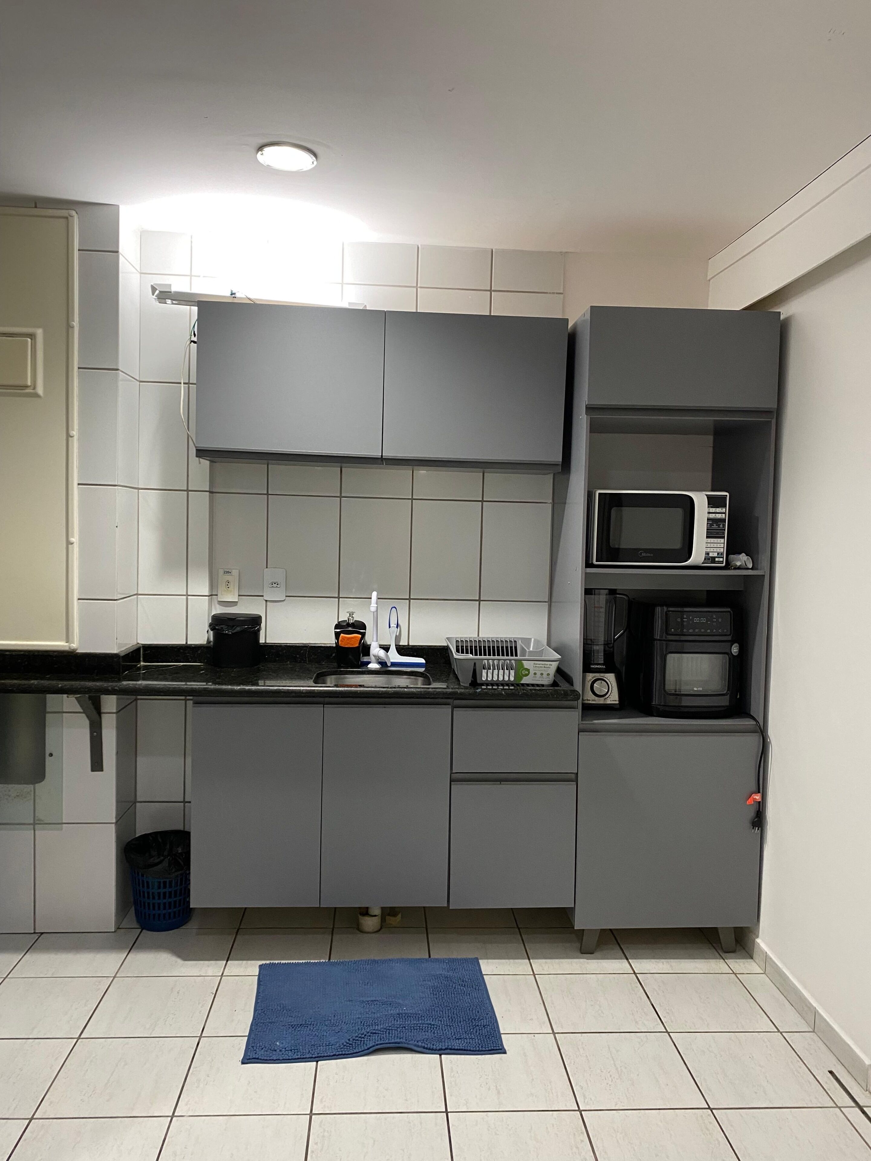Una cocina compacta con armarios grises, un microondas y un lavamanos.