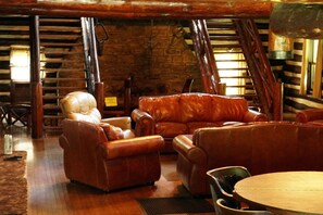 A rustic interior with leather sofas, a wooden table, and a stone wall.