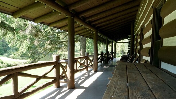 A covered outdoor seating area with wooden benches and a railing, overlooking a natural landscape. - Amazing 6+-bedroom lodge in Spring Mills perfect for group getaways. (Spring Mills)