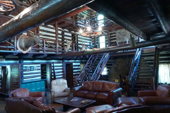 A rustic interior with wooden beams, leather furniture, and antlers mounted on the ceiling.