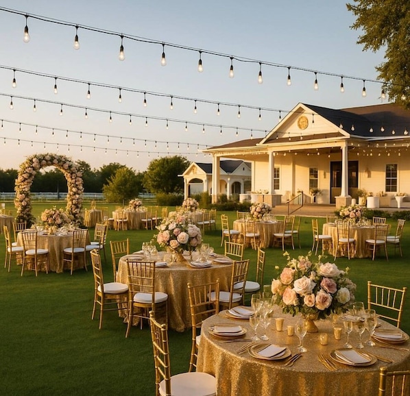 An outdoor wedding reception with round tables, gold chairs, and string lights.