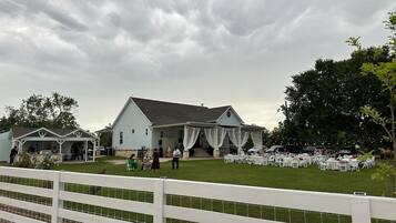 A large building with a covered outdoor area, surrounded by a white fence, and a grassy lawn.