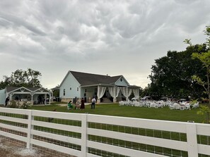 A large building with a covered outdoor area, surrounded by a white fence, and a grassy lawn.