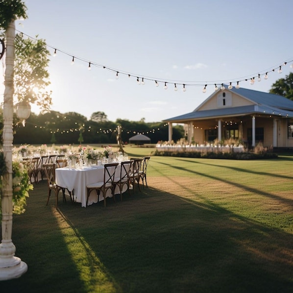 An outdoor wedding venue with string lights, tables set for guests, and a building in the background.