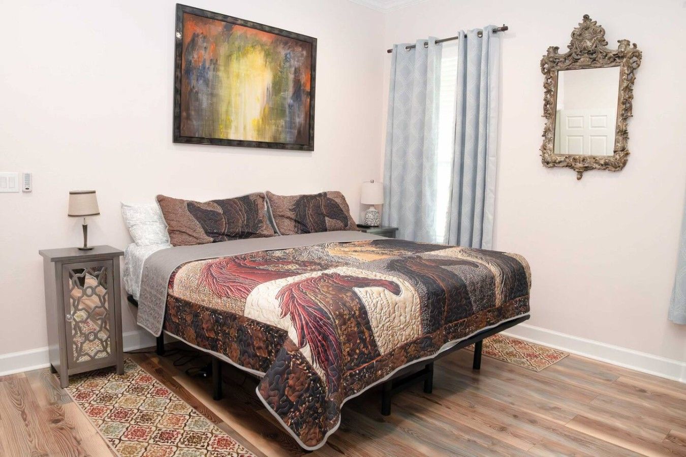 A bedroom with a bed, a nightstand, a lamp, a painting, a mirror, and a window with curtains.