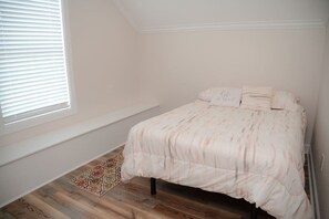 A bedroom with a bed, a window with blinds, a patterned rug, and a radiator.