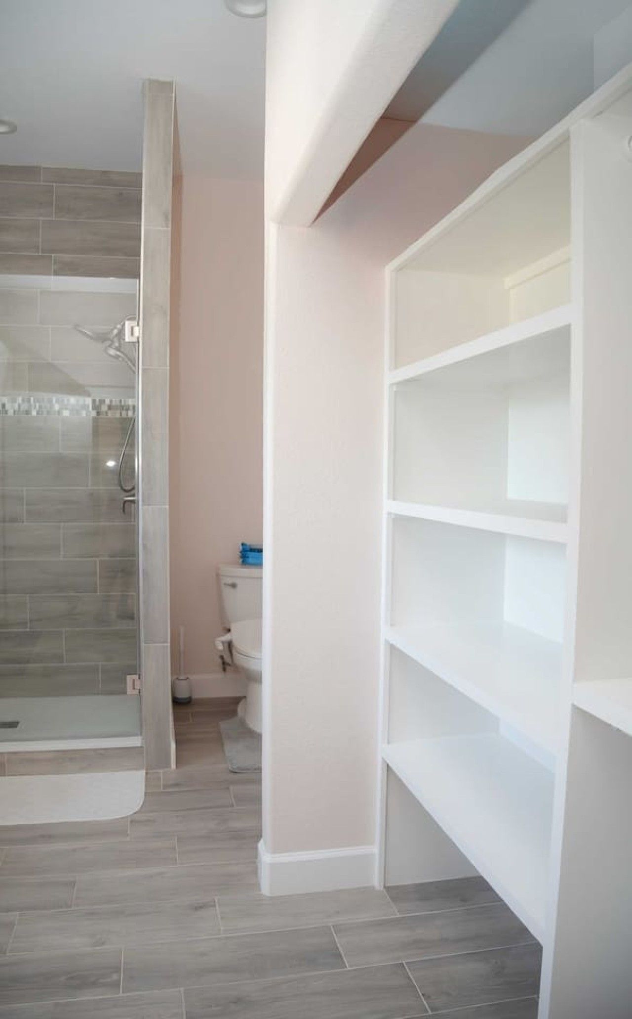 A bathroom with a shower, toilet, and storage shelves.