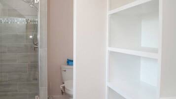 A bathroom with a shower, toilet, and storage shelves.