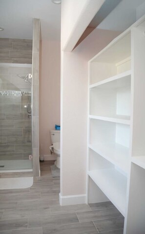 A bathroom with a shower, toilet, and storage shelves.