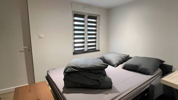 Un dormitorio compacto con una cama plegable, una mesita de madera y una ventana con persianas.