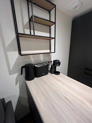 Une petite cuisine équipée d’un plan de travail en bois, d’une machine à café, d’un grille-pain et d’une tasse noire.