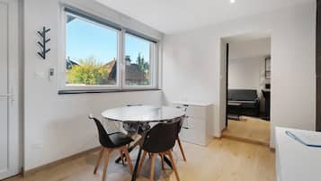 Een moderne eethoek met een ronde tafel, twee stoelen en een raam met uitzicht op gebouwen en bomen.