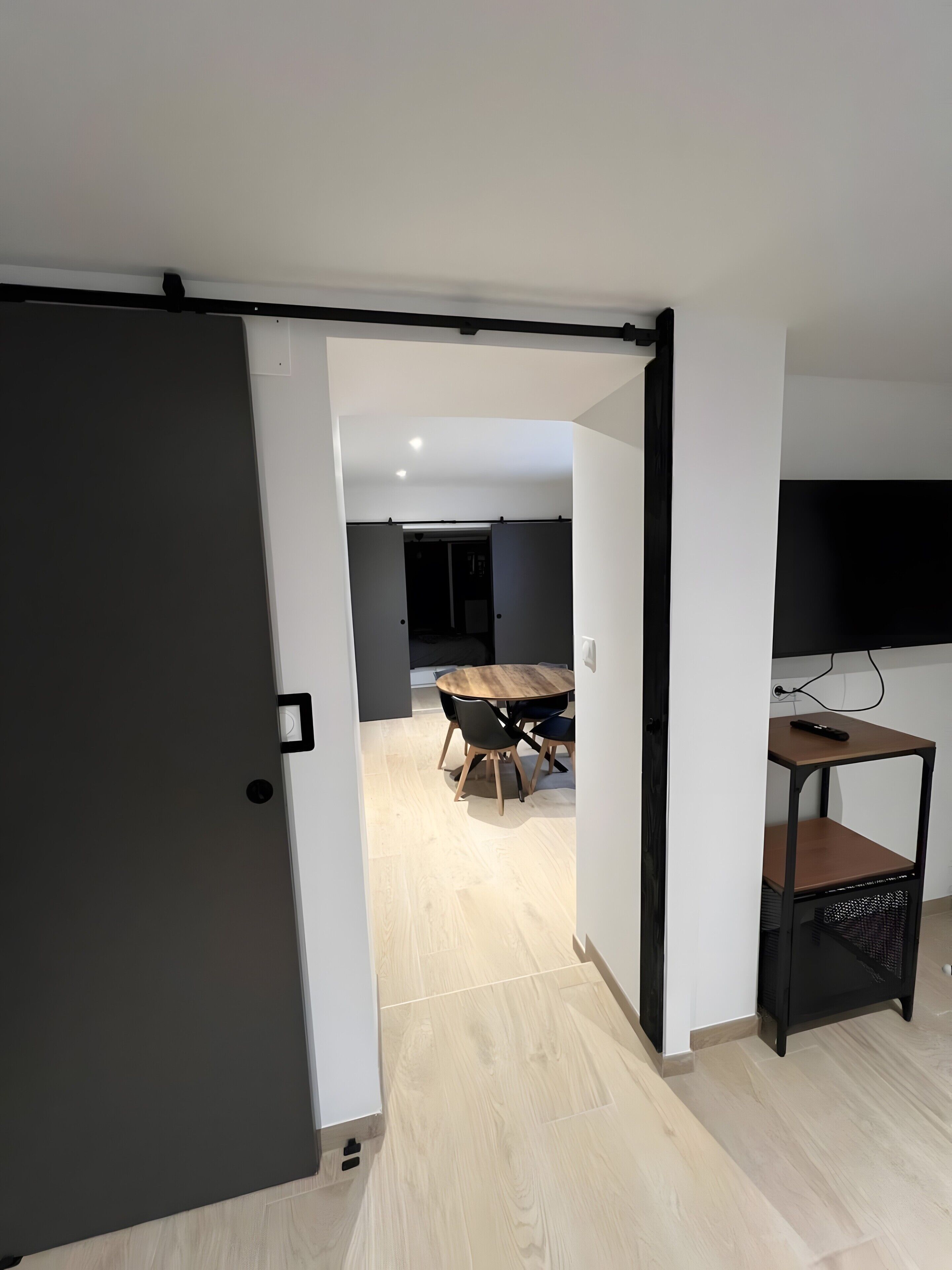 Ein modernes Interieur mit Essbereich, einem an der Wand montierten Fernseher und einer Schiebetür zu einem weiteren Raum.