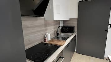 Una cocina moderna con una placa de inducción negra, un microondas y una tabla de cortar de madera.