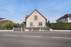 Une maison à deux étages, dotée d’un toit à deux versants, d’un portail à l’avant et d’une haie bien entretenue.