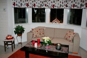 Ein Wohnzimmer mit einer Couch, einem Couchtisch, einer Pflanze und einem Fenster mit Vorhängen.