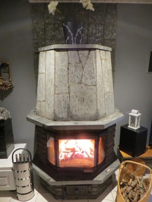 Ein Steinkamin mit Feuer, eine Vase mit Blumen darauf und ein Holzkorb daneben.