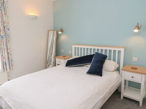 Ein Schlafzimmer mit einem Bett, zwei Nachttischen, einem Spiegel und einer Wandleuchte.