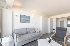 Uma sala de estar moderna com um sofá cinzento, uma cadeira de madeira e uma mesa de centro branca.