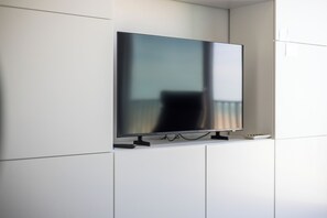 Televisão de tela plana fixada em um armário branco, com um cabo passando por baixo.