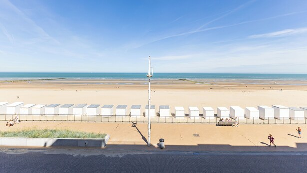 A beach with a row of white beach huts, a clear sky, and a calm sea. - 1 bedroom accommodation in Koksijde (Koksijde)