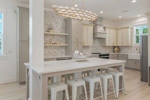 A modern kitchen with a central island, white bar stools, and a decorative light fixture. - Beacon: 30A beaches, sleeps 26, private pool! (Santa Rosa Beach)