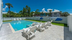 A swimming pool with lounge chairs and surfboards, surrounded by a fence and palm trees. - Beacon: 30A beaches, sleeps 26, private pool! (Santa Rosa Beach)