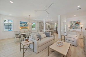 A spacious living room with a sofa, coffee table, and dining area. - Beacon: 30A beaches, sleeps 26, private pool! (Santa Rosa Beach)