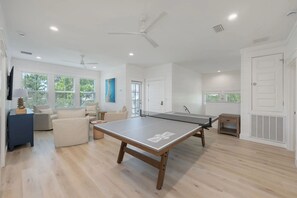Ein geräumiger Raum mit einem Tischtennis-Tisch, einer Sitzecke mit Stühlen und einem Deckenventilator.
