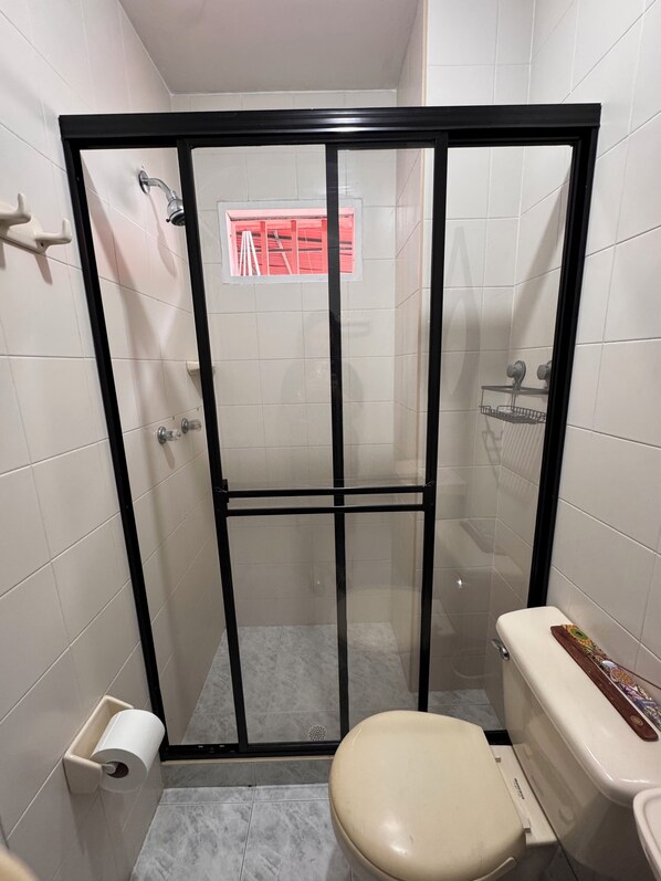 A small bathroom with a toilet, a shower stall with a glass door, and a toilet paper holder.