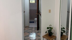 A hallway with a tiled floor, a door leading to a bathroom, and a small table with a plant.