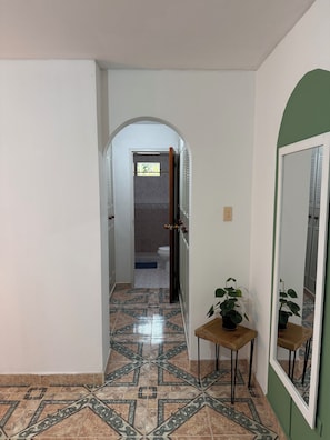 A hallway with a tiled floor, a door leading to a bathroom, and a small table with a plant.