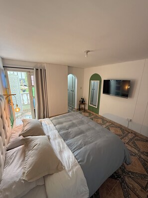Ein Schlafzimmer mit einem Bett, einem an der Wand befestigten Fernseher und Blick ins Freie.