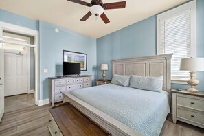 A bedroom with a bed, a ceiling fan, a dresser, a television, and a window with blinds. - Kiva Village A 201 - Luxury 3BR Golf-front Condo With Kiva Beach Club Access (Gulf Shores)
