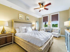 A bedroom with a bed, nightstands, a chair, a ceiling fan, and windows with blinds. - Kiva Village A 105 - Golf Course Views & Luxury Beach Club Access at Kiva Village (Gulf Shores)
