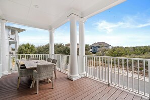 A covered outdoor area with a table and chairs, white columns, and a view of a residential area. - Stones Throw - Luxury 5BR Beach Retreat at Kiva Dunes With Private Beach Club (Gulf Shores)