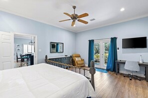 Ein Schlafzimmer mit Bett, Schreibtisch, Stuhl, Fernseher und Deckenventilator.