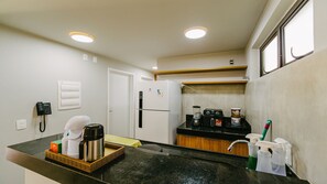 Eine kleine Küche mit Kühlschrank, Kaffeemaschine und Telefon auf der Arbeitsfläche.