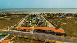 An aerial view of a resort with multiple buildings, a swimming pool, and a road in the foreground. - Resort Apartment with Access to Coqueiro Beach (Luís Correia)