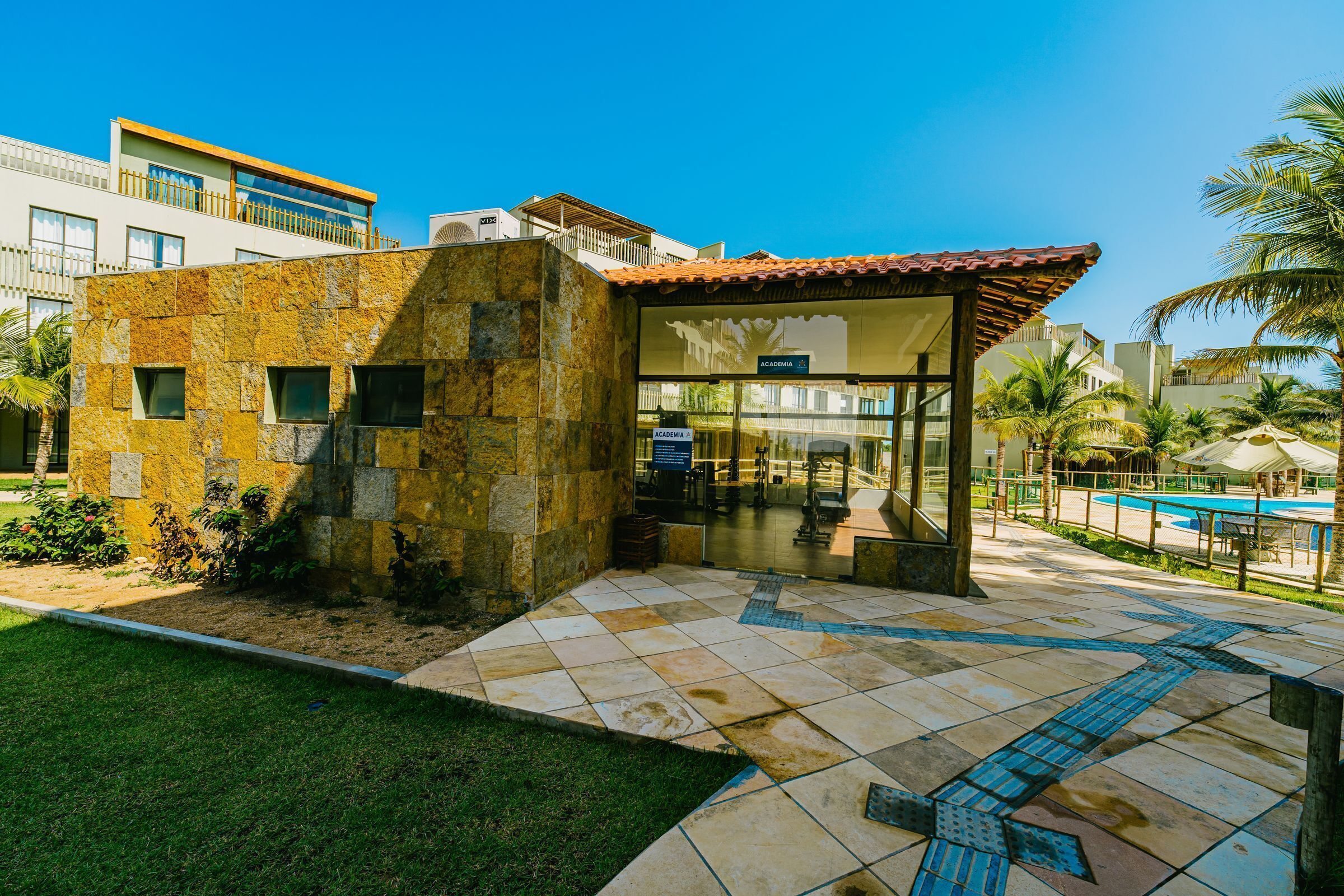 Um edifício moderno com fachada de pedra, entrada de vidro e área de piscina.