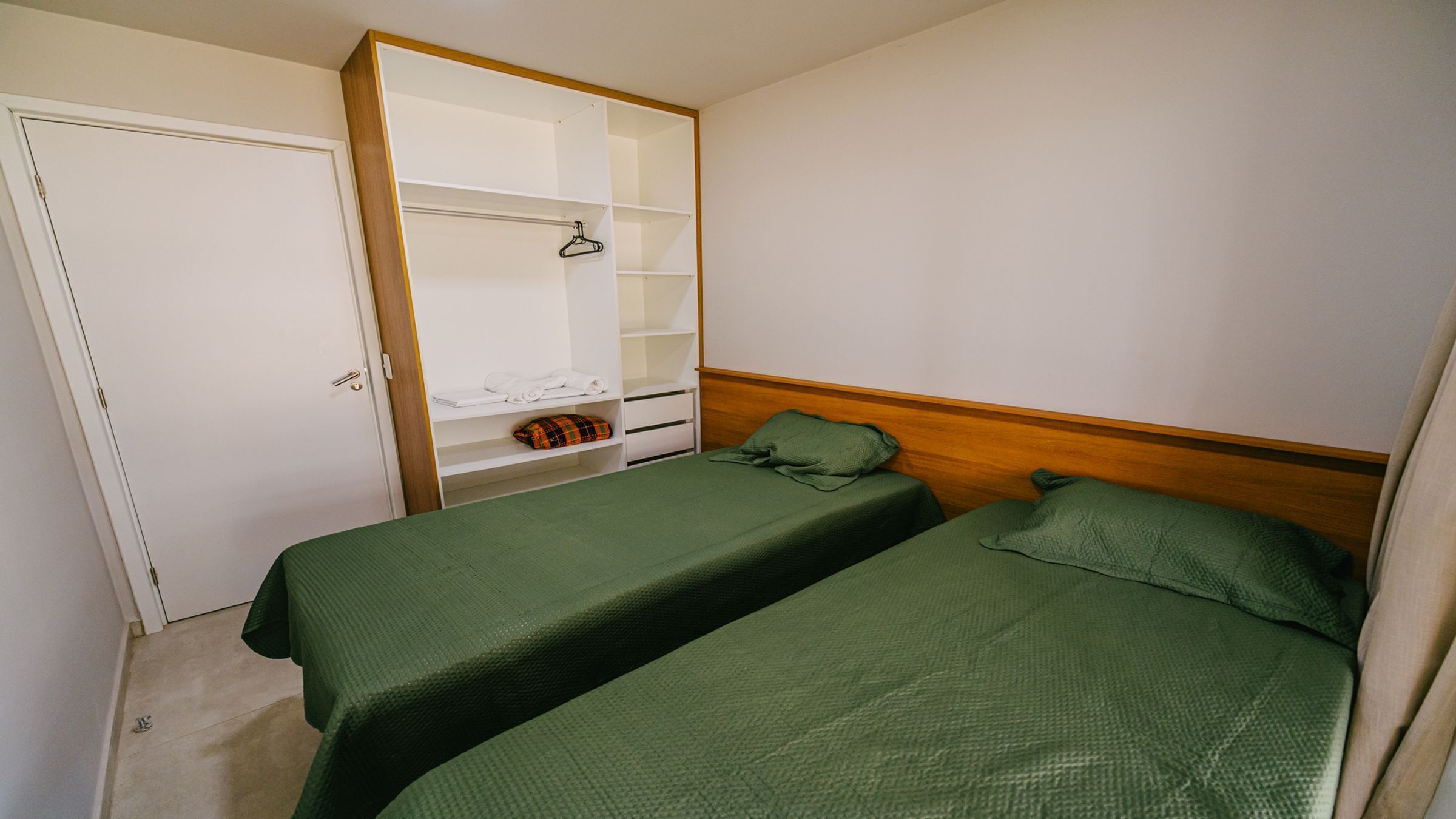 A small, single-room accommodation with two beds, a wardrobe, and a shelf unit.