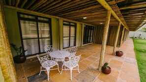 A covered patio area with a table and chairs, potted plants, and a sign indicating the location. - Resort Apartment with Access to Coqueiro Beach (Luís Correia)