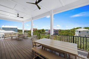 Eine überdachte Terrasse mit Tisch und Stühlen, einem Deckenventilator und Blick auf umliegende Gebäude.