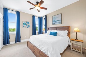 A bedroom with a bed, a nightstand, a lamp, a ceiling fan, and a window with curtains. - Kiva Village A 305 - Golf-front Luxury Retreat Beach Club & Private Beach Access (Gulf Shores)