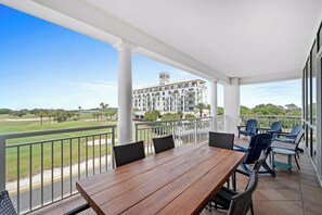 A covered outdoor area with a wooden table and chairs, overlooking a golf course and a building with multiple balconies. - Kiva Village A 305 - Golf-front Luxury Retreat Beach Club & Private Beach Access (Gulf Shores)