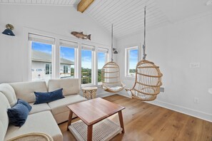 A spacious living room with a sofa, a coffee table, and two hanging chairs. - Blue Skies: Renovated Gulf Coast Retreat Steps From Beach & Pool (Gulf Shores)