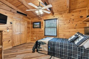 A wooden cabin room with a bed, a ceiling fan, a window, and a door. - Breezy Creek Retreat-Spectacular Waterfront Cabin! (Maggie Valley)