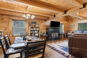Ein Interieur einer Holzhütte mit Essbereich, Kamin und Sitzgelegenheiten.