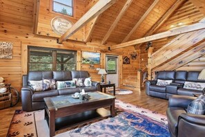 Ein Holzblockhaus-Interieur mit zwei Ledersofas, einem Couchtisch und einem großen Fenster mit Jalousien.